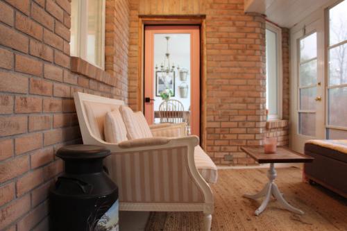 a porch with a white rocking chair and a brick wall at Romantic Waterfront Sunset Views in PEC in Belleville