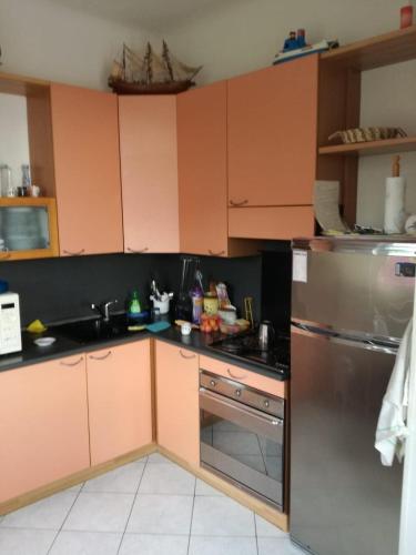 La cuisine est équipée de placards orange et d'un réfrigérateur en acier inoxydable. dans l'établissement Menton apartment with large terrace, à Menton