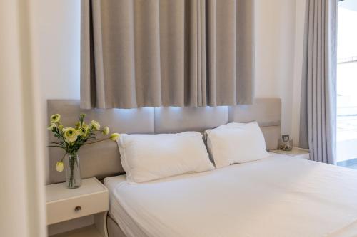 a bedroom with a white bed with a vase of flowers at Hotel Myrtai - City Center in Sarandë
