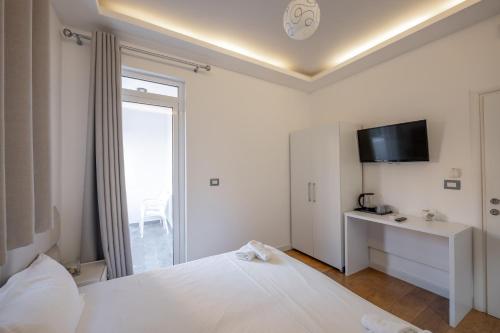a white bedroom with a bed and a television at Hotel Myrtai - City Center in Sarandë