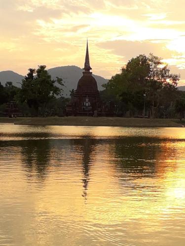 a building with a reflection in the water with a church at Toon Guesthouse in Sukhothai