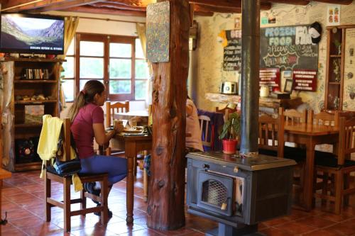 a woman sitting at a table with a wood stove at Hostel El Mirador in El Bolsón