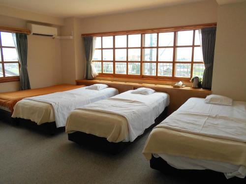um quarto de hotel com três camas e janelas em Orange Pension em Gamagori