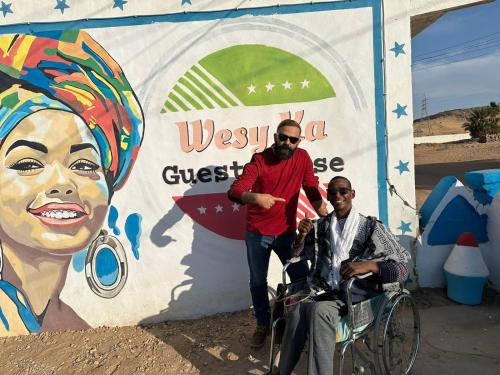 a man and two men in wheelchairs in front of a wall at Wesy Ka Guest House in Aswan