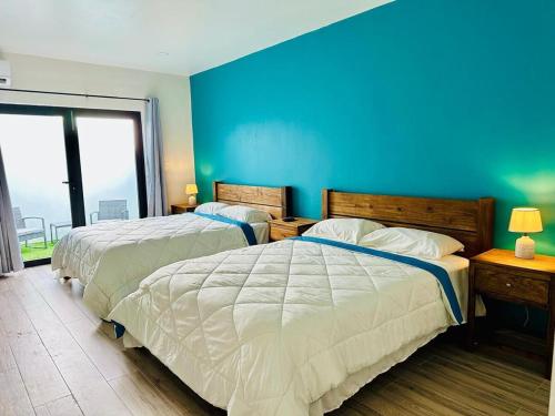 two beds in a bedroom with a blue wall at Eagle Stays Aruba-NEW Luxurious One Bedroom Apartment Near Eagle Beach! in Oranjestad