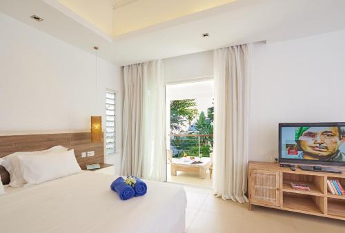 a white bedroom with a bed and a television at Le Beachclub in Pereybere