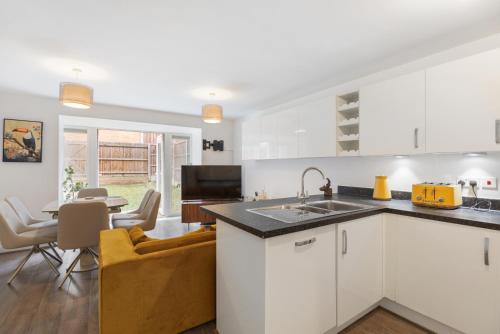 a kitchen with white cabinets and a dining room at Pristine house near Dartford Station with Free Parking and Study in Dartford