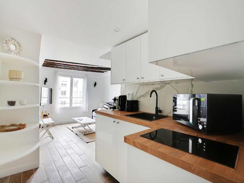 a kitchen with white cabinets and a black microwave at Charming studio near les Halles - Mobility lease in Paris