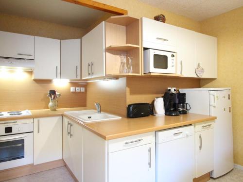 une cuisine avec des armoires blanches, un évier et un micro-ondes dans l'établissement Duplex central 90m² avec parking, 2 chambres, 6 couchages, proche Thermes, wifi inclus - FR-1-415-136, à Le Mont-Dore