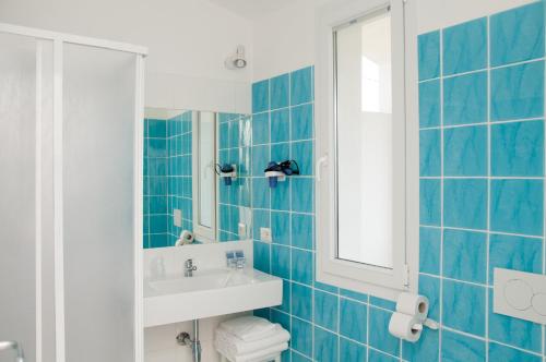La salle de bains est pourvue de carrelage bleu, d'un lavabo et d'un miroir. dans l'établissement Meta Hotel, à Santa Teresa Gallura