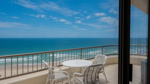 a balcony with a table and chairs and the ocean at Norfolk Luxury Beachfront Apartments Gold Coast in Gold Coast