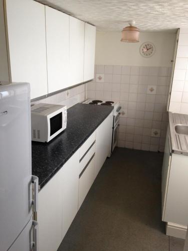 a small kitchen with white cabinets and a microwave at Isambard Cottage in Weymouth