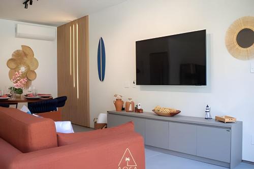 a living room with a couch and a tv on a wall at Villa Naluri - Seu Refúgio a 50 metros da praia em Japaratinga in Japaratinga