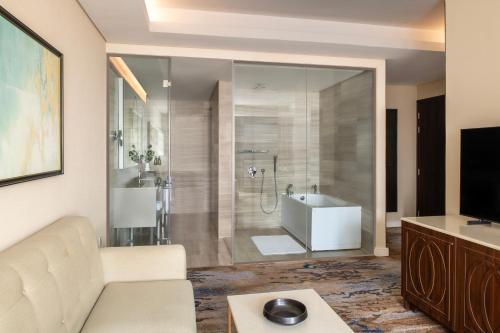 a living room with a couch and a bathroom with a shower at Dusit Doha Hotel in Doha