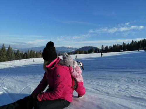 a woman and a child sitting on the snow at Kwatera Na Śliwkowej in Zabrzeg