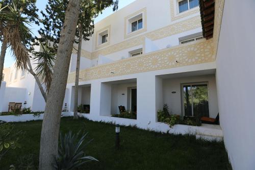 a white building with a palm tree in the yard at Le Caid Hotel in Bou Saâda