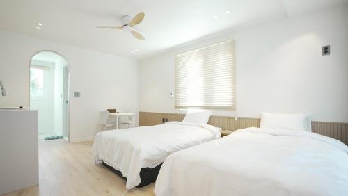 two beds in a white room with a ceiling fan at Stay Yongdam in Jeju