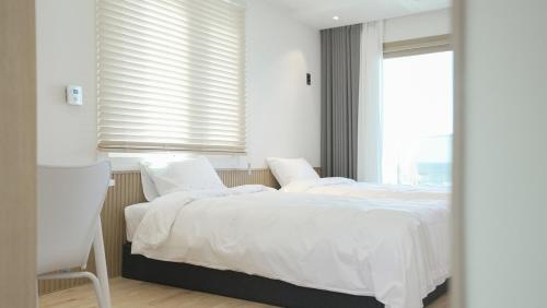 a bedroom with two beds with white sheets and a window at Stay Yongdam in Jeju