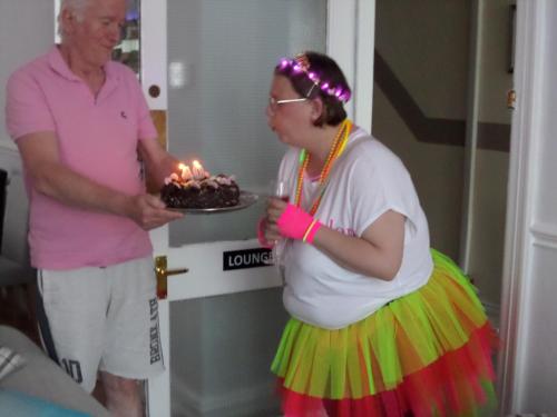a woman in a colorful dress holding a cake with lit candles at Nathans in Blackpool