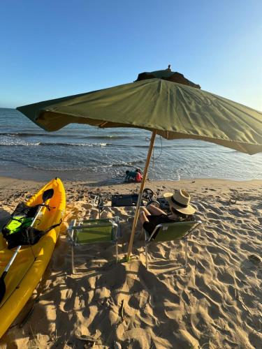 a beach with an umbrella and a kayak on the sand at Malie Bangalô - Alagoas in Barra de Santo Antônio