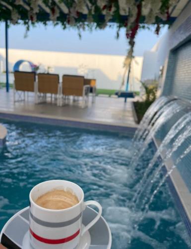 a cup of coffee sitting on a plate next to a pool at almourooj chalet in Ḩalbān