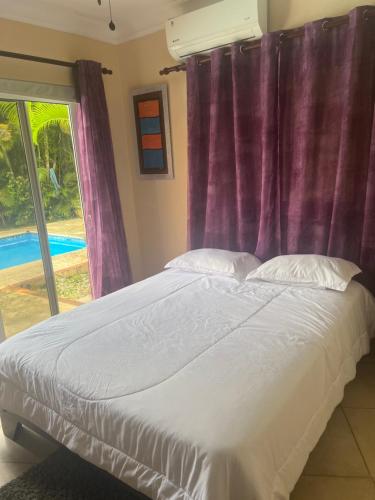a bedroom with a bed with purple curtains and a window at Casa Linda beautiful Villa in Sosúa