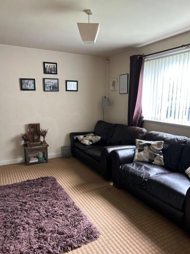 a living room with a black leather couch and a rug at Cosy 3 bedroom house to rent in Manchester