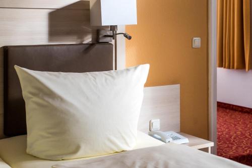 a bed with a pillow and a phone on a table at Hotel Gorch Fock in Timmendorfer Strand