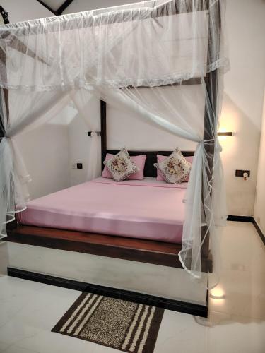 a bedroom with a canopy bed with pink pillows at Nice View Safari villa in Udawalawe