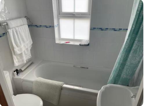 a white bathroom with a tub and a toilet and a window at April Cottage Ringwood in Ringwood