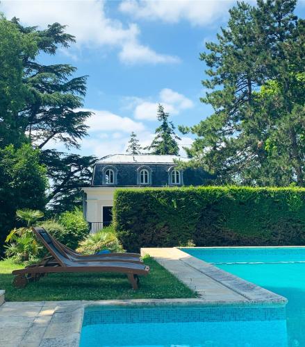 un banc à côté d'une piscine en face d'une maison dans l'établissement Hôtel Le domaine de Montmorency, à Montmorency
