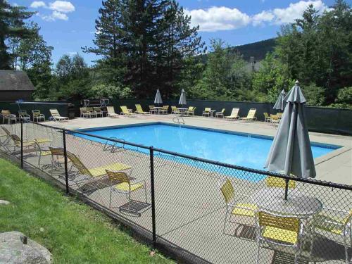 a fence around a swimming pool with chairs and an umbrella at Cozy Ski Condo in Waterville Valley