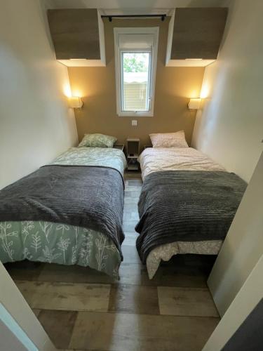 two beds in a small room with a window at Mobilhome bord du lac in Parentis-en-Born