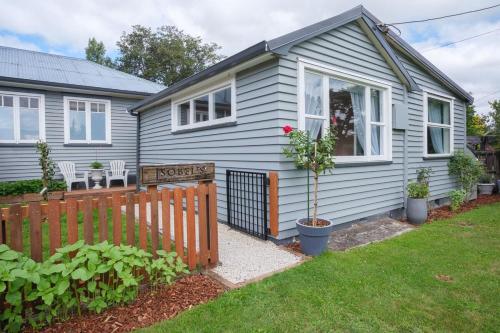 a blue house with a fence and a yard at Isobel's Rose Cottage in Hanmer Springs