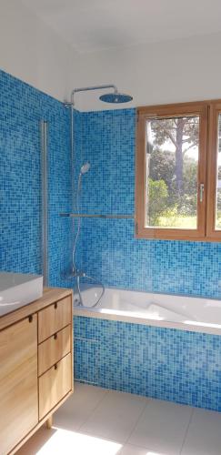 - une salle de bains carrelée de bleu pourvue d'une baignoire et d'une fenêtre dans l'établissement Havre de paix à 10 minutes de la mer et 15 minutes d'Ajaccio, à Appietto