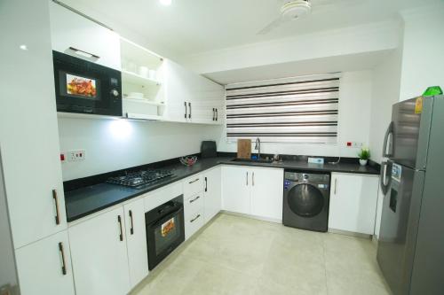 Una cocina con gabinetes blancos y lavadora y secadora. en Kenji with Balcony & Gym 410, en Oyarifa