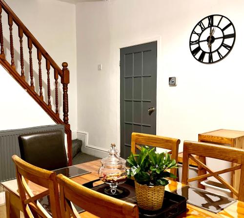 a dining room with a table and a clock on the wall at Cosy 3BDR In Levenshulme-Close To Manchester City Centre And Stockport Town- Free Parking- WiFi in Manchester