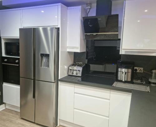 a kitchen with a stainless steel refrigerator and white cabinets at Uniq 3 Bedroom House in central Watford ,15min to London Euston , close to Harry Potter in Watford