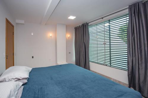 a bedroom with a blue bed and a large window at Sobrado Luxo com Hidromassagem, Terraço e Lareira in Maringá