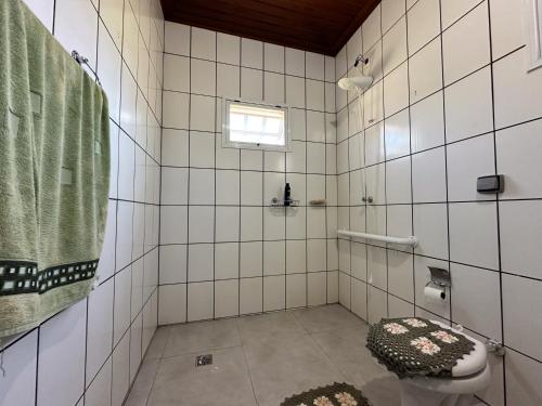 a white tiled bathroom with a toilet and a window at Sítio Canto da Seriema in Torrinha