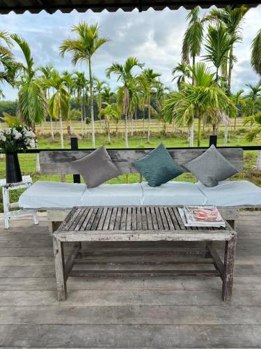 a wooden bench with pillows on a patio with palm trees at นาน้าหมูฟาร์มสเตย์ NanamooFarmStay in Trang