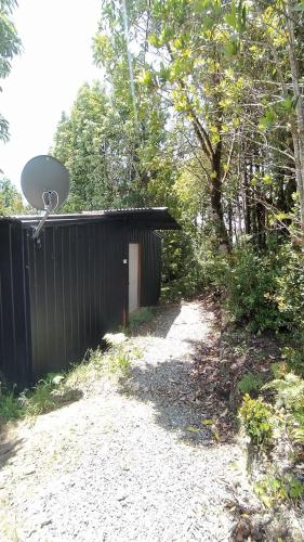 a black building with a door next to a dirt road at Cabañas del Escultor Cabaña Canelo in Valdivia