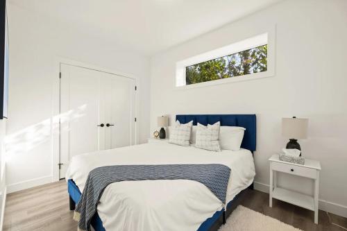 a white bedroom with a bed and a window at Cozy Saanich Cottage ideal location to UVIC and Downtown in Victoria