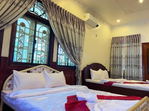 two beds in a room with two windows at Lotus Blanc Homestay Village in Battambang