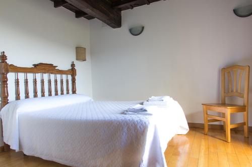 een slaapkamer met een wit bed en een houten stoel bij Casa do Comediante in Cerdeira