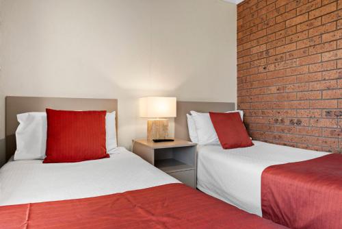 two beds with red pillows in a hotel room at Bomaderry Motor Inn in Nowra