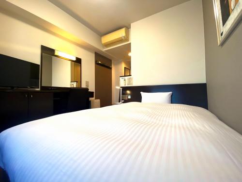 a bedroom with a white bed and a television at Hotel Route-Inn Ashikaga Ekimae in Ashikaga