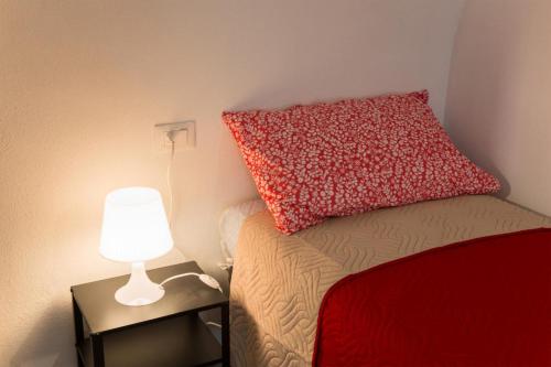 a bed with a red pillow and a lamp on a table at Casa Margherita PT, Borno Ospitar in Borno