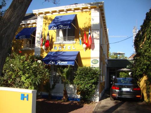 un coche aparcado frente a un edificio amarillo con sombrillas azules en Hotel Las Flores, en Santiago
