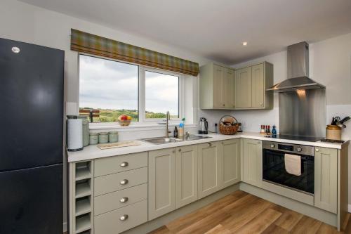 une cuisine avec des armoires blanches et un réfrigérateur noir dans l'établissement Armadale Farm Cottage, à Armadale